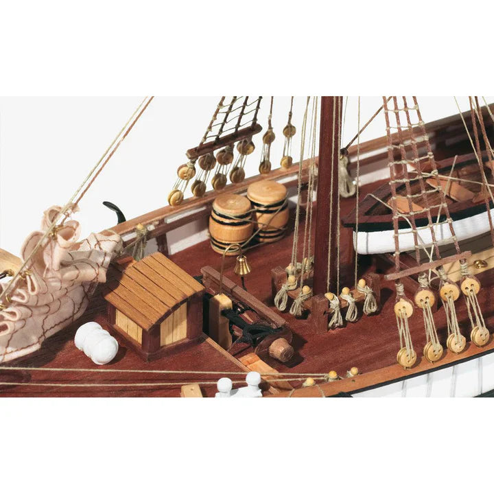 Close-up of OcCre 13001 Aurora wooden ship model kit, 1:65 scale, showing detailed deck fittings, wooden barrels, rigging blocks, ropes, and mast.