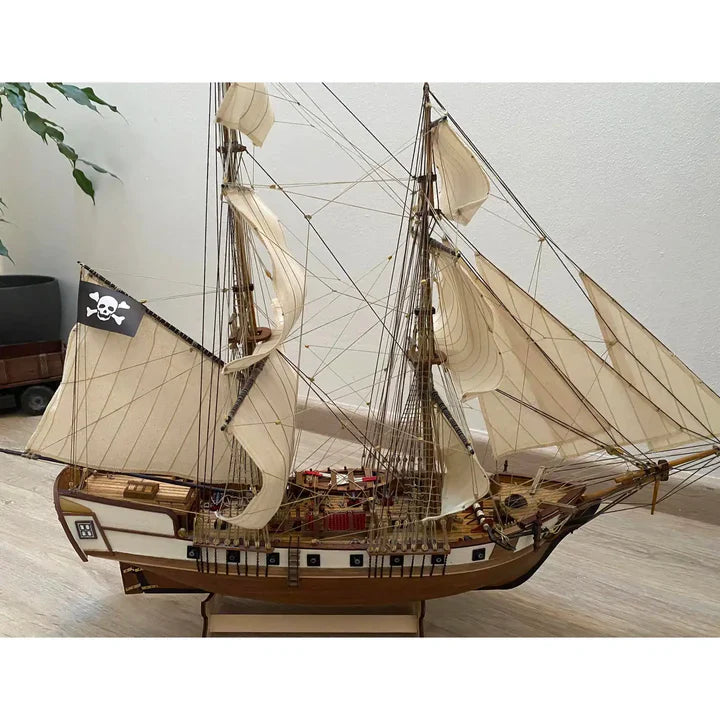Completed OcCre Corsair 1:80 scale wooden pirate ship model featuring detailed rigging, cream-colored sails, wooden hull, and Jolly Roger pirate flag